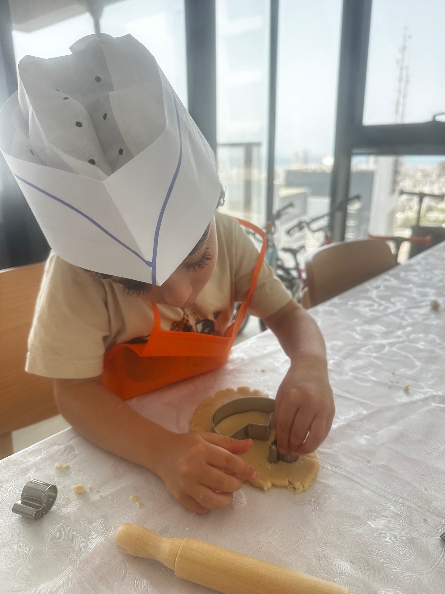 A boy in a paper chef hat using a cookie cutter