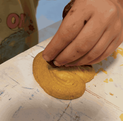 A child's hands squeezing melted chocolate from a snipped sandwich bag onto a cookie