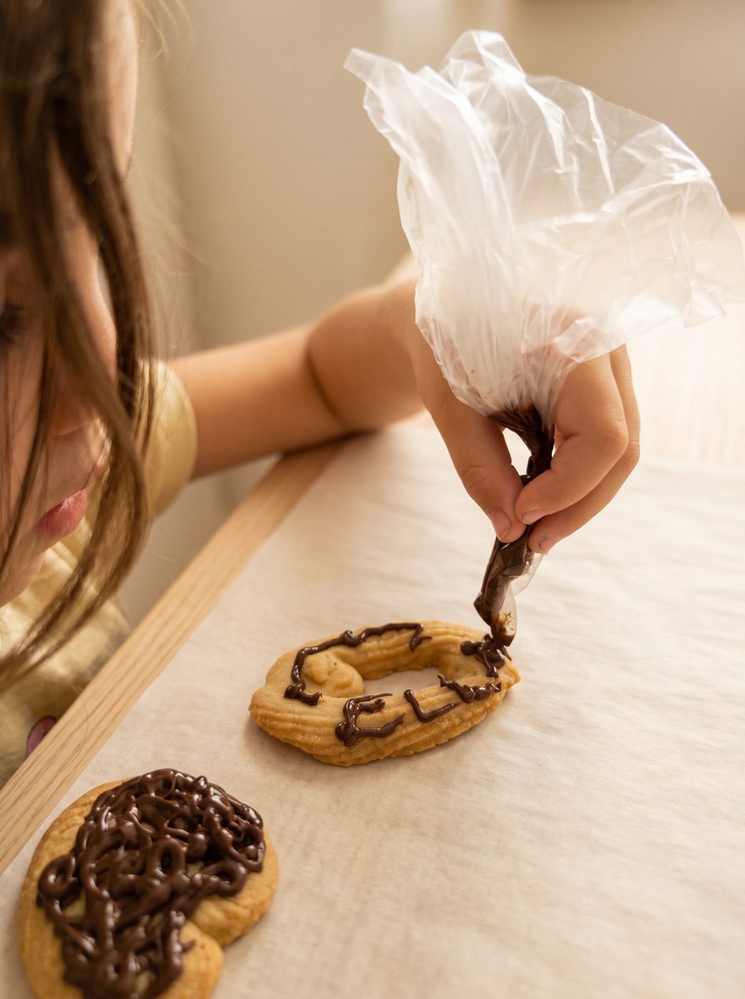 A child piping chocolate letters onto a butter cookie on baking parchment
