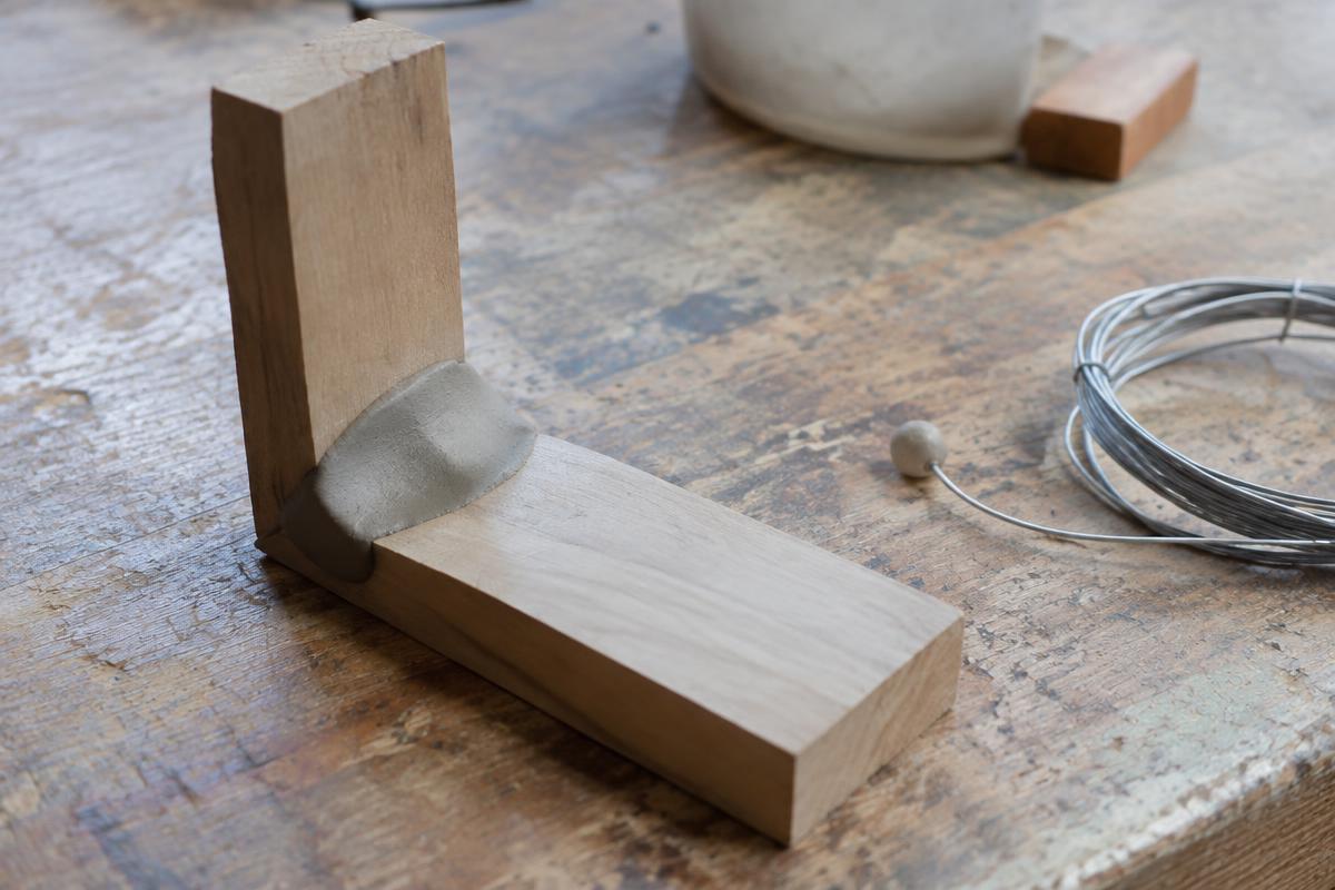 Two wooden blocks joined with a blob of grey clay, beside a coil of wire with a clay ball on its end