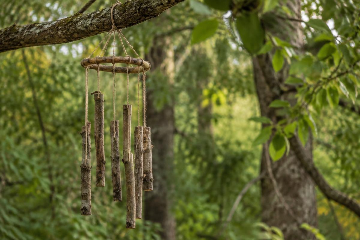 A handmade wind chime of thin wooden twigs hanging on threads from a tree branch