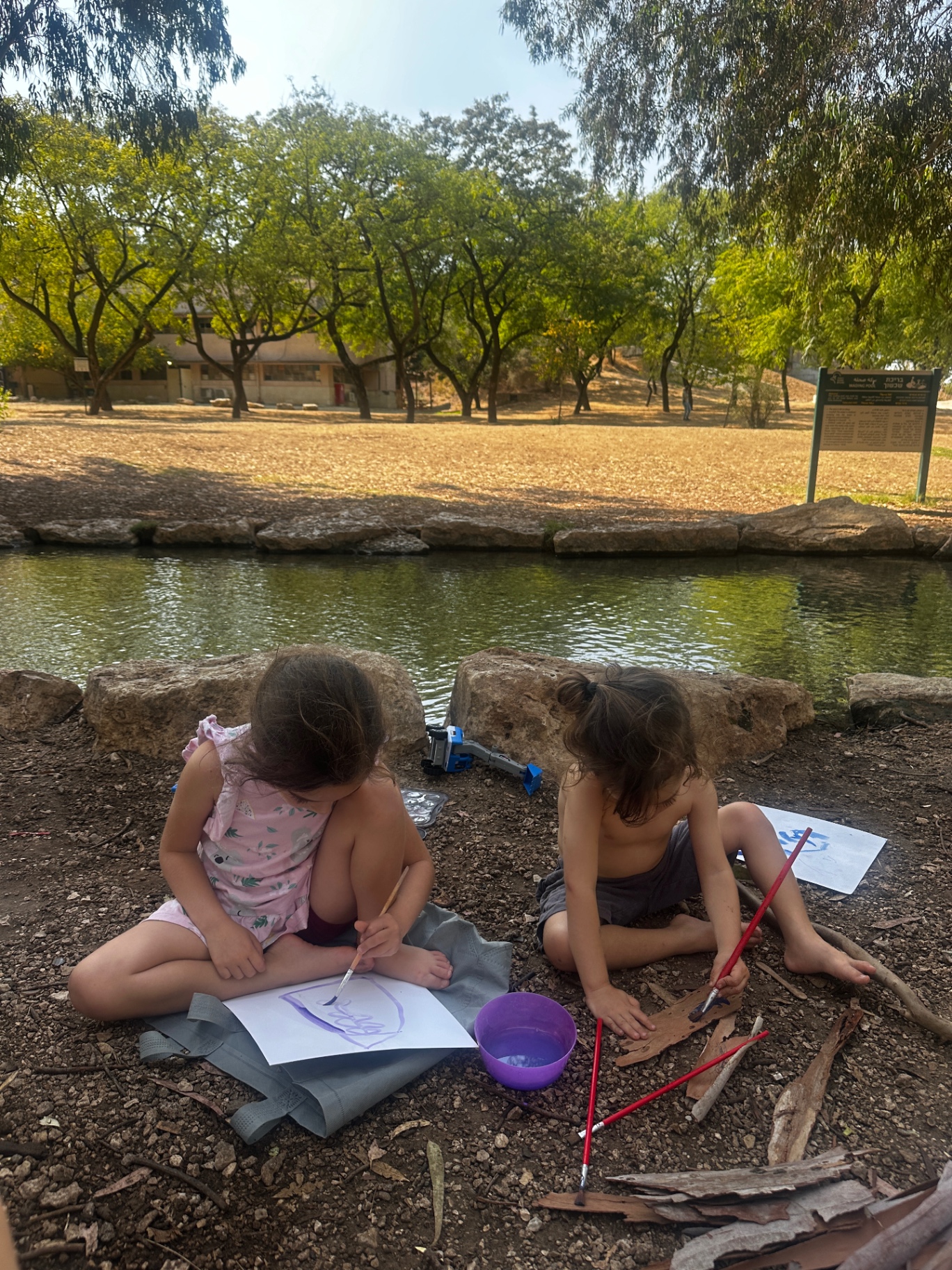 Two children painting with water by a pond