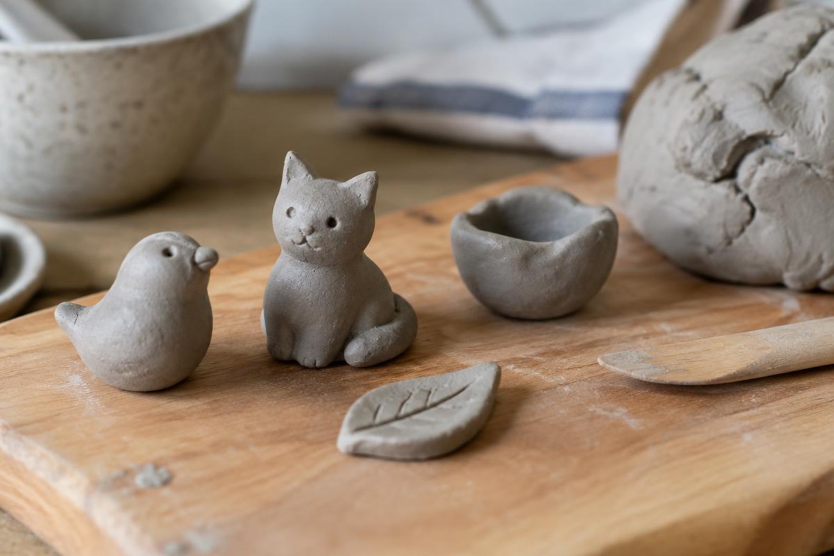 Small hand-shaped air-dry clay animals drying on a wooden board next to a lump of soft clay