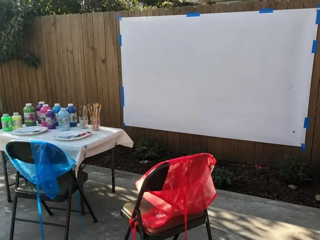 A big sheet taped to the fence, paints and aprons ready. A vertical surface changes everything.