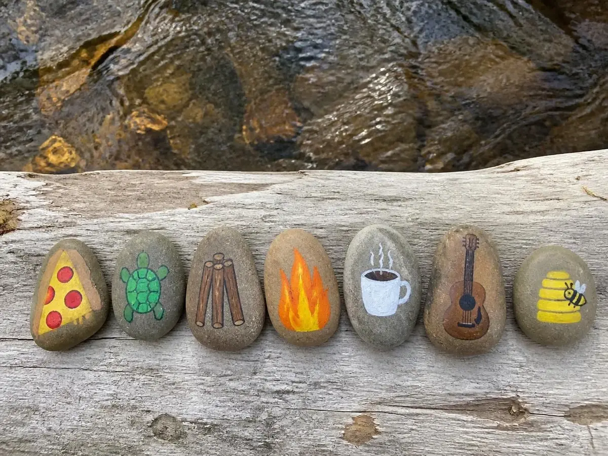 Our creek-side set: pizza, turtle, sticks, campfire, coffee cup, guitar and beehive — a whole pretend world in stones.