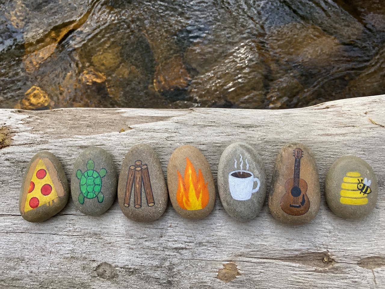Our creek-side set: pizza, turtle, sticks, campfire, coffee cup, guitar and beehive — a whole pretend world in stones.